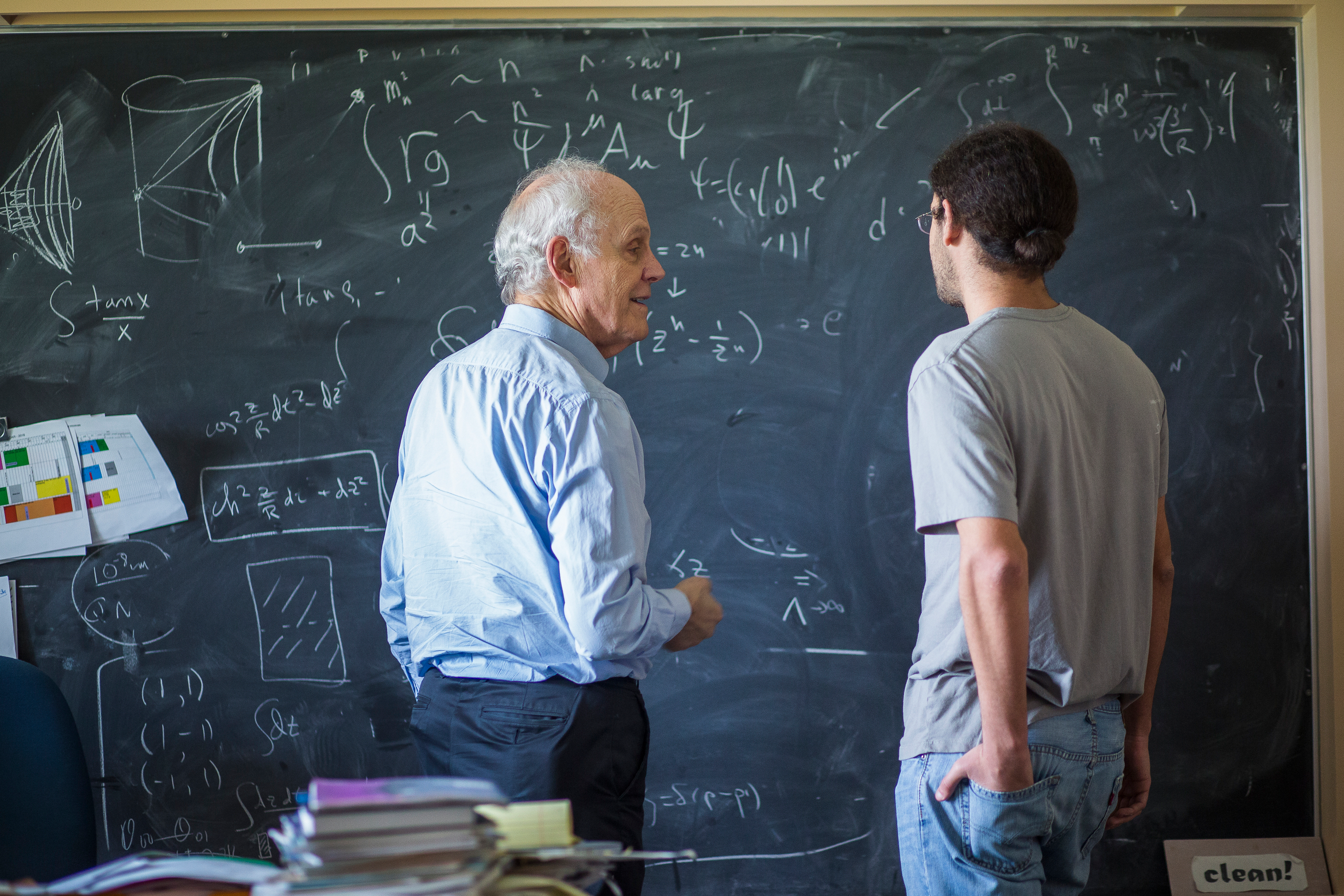 Two persons standing infront of a chalkboard with mathematical equations written on it